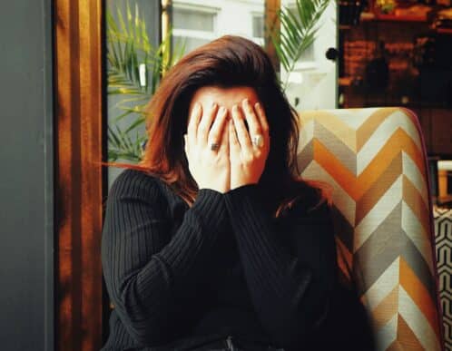 Chica con las manos en la cara tapándose los ojos.